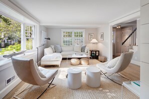 A modern living room with a white sofa, two armchairs, a coffee table, and a large window with blinds.