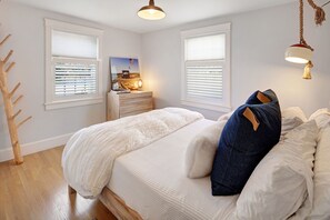 Ein Schlafzimmer mit einem großen Bett, zwei Fenstern mit Jalousien, einem Nachttisch mit Lampe und einer Holzskulptur eines Baumes.