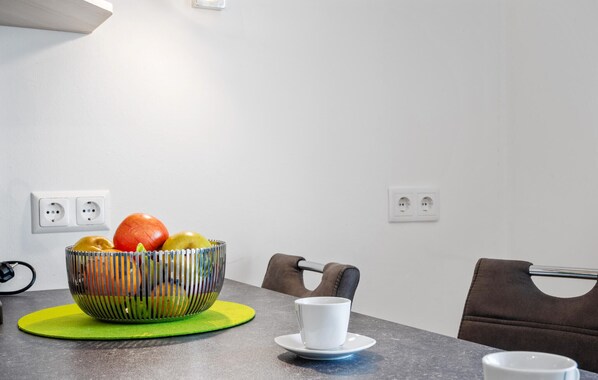 A dining table with a fruit bowl, a white cup, and a green placemat.
