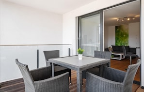 A balcony with a table and chairs, a potted plant, and a view of the interior.