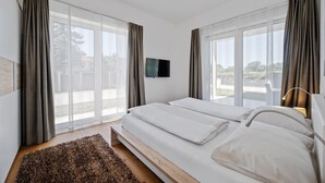 A modern hotel room with a large bed, a flat-screen TV, and large windows with curtains. - 2 bedroom awesome apartment in Pörtschach am Wörtherse (Pörtschach am Wörtherse)