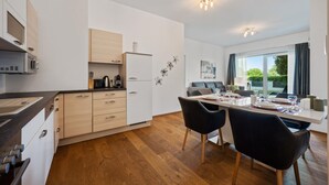 A modern kitchen with wooden cabinets, a dining area with two black chairs, and a large window offering a view of greenery outside. - 2 bedroom awesome apartment in Pörtschach am Wörtherse (Pörtschach am Wörtherse)
