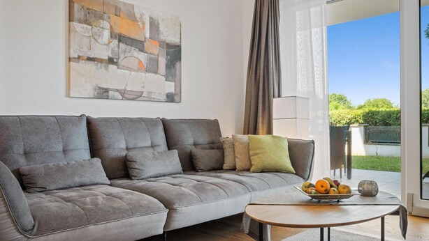 A modern living room with a grey sofa, a coffee table with fruits, and a large abstract painting on the wall. - 2 bedroom awesome apartment in Pörtschach am Wörtherse (Pörtschach am Wörtherse)