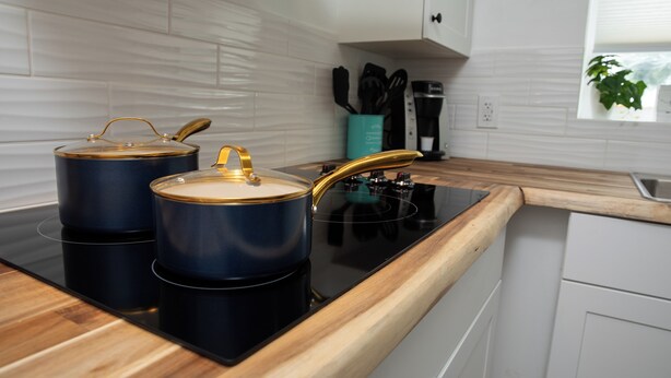 A modern kitchen with a black induction cooktop, two stainless steel pots with lids, and a wooden countertop. - Bright and Cozy Basement Oasis in the Minnow Lake area (Greater Sudbury)