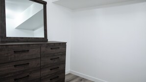 A room with a dark wooden dresser, a large mirror, and white walls. - Bright and Cozy Basement Oasis in the Minnow Lake area (Greater Sudbury)