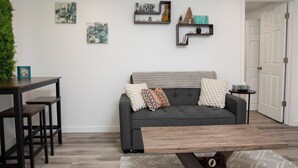 A living room with a grey sofa, wooden coffee table, and a dining area with a wooden table and benches. - Bright and Cozy Basement Oasis in the Minnow Lake area (Greater Sudbury)