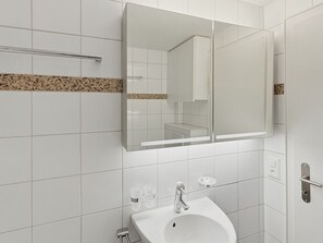 A bathroom with white tiles, a sink, a mirror, and a towel rack. - Charming Studio in the old town - UZ15 (Zürich)