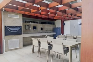 A modern kitchen with a central island, built-in appliances, and a seating area with chairs and a table. - Flat pé na areia branco Haus My flats  (Joao Pessoa)