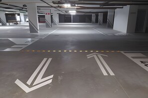 Un estacionamiento subterráneo con flechas direccionales en el piso, pilares de concreto e iluminación colgante.