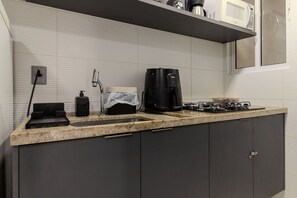A kitchen with a gas stove, a coffee maker, a microwave, and a sink. - Flat pé na areia branco Haus My flats  (Joao Pessoa)
