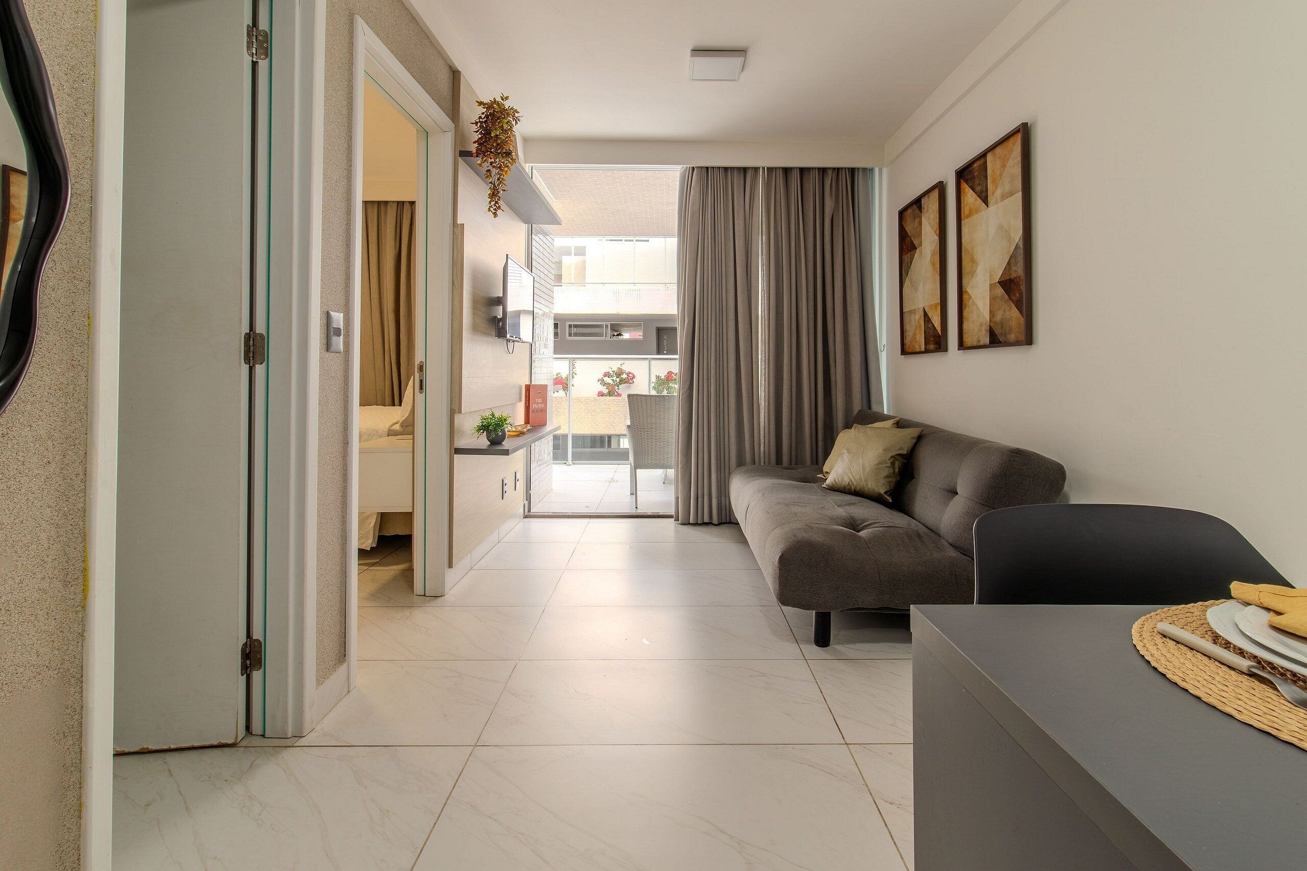 A modern living room with a sofa, a dining table, and a kitchen area visible through an open door.