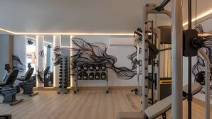 Gimnasio con equipamiento de ejercicio, espejos y piso de madera.