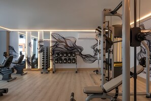 Gimnasio con equipamiento de ejercicio, espejos y piso de madera.