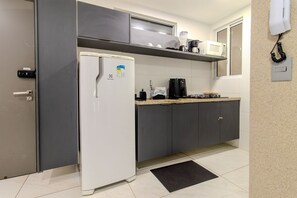 Una cocina compacta con un refrigerador blanco, un microondas, una estufa a gas y una cafetera.
