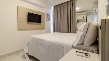 A hotel room with a bed, a TV mounted on a wooden panel, a bedside table with a remote control, and a wardrobe.