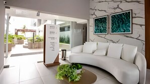 Una sala de estar moderna con un sofá blanco, una mesa de centro con plantas y una pared con estampado de mármol.