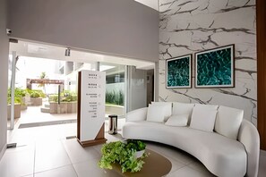 Una sala de estar moderna con un sofá blanco, una mesa de centro con plantas y una pared con estampado de mármol.