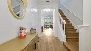 Ein Flur mit Holzboden, einer weißen Tür und einer Treppe mit weißen Geländern.