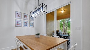 Ein Essbereich mit Holztisch und weißen Stühlen, einer h ängenden Leuchte und gerahmten Postern an der Wand.