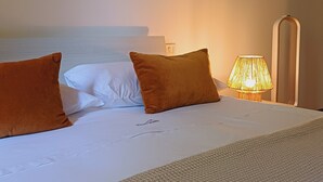 A neatly made bed with white and brown pillows, a textured white bedspread, and a bedside lamp with a striped lampshade.