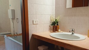A bathroom with a bathtub, a sink, and a mirror. There are towels and a plant on the counter.