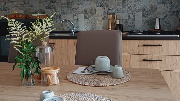 A modern kitchen with wooden cabinets, a tiled backsplash, and a dining area set with a table, chairs, and a coffee setup.