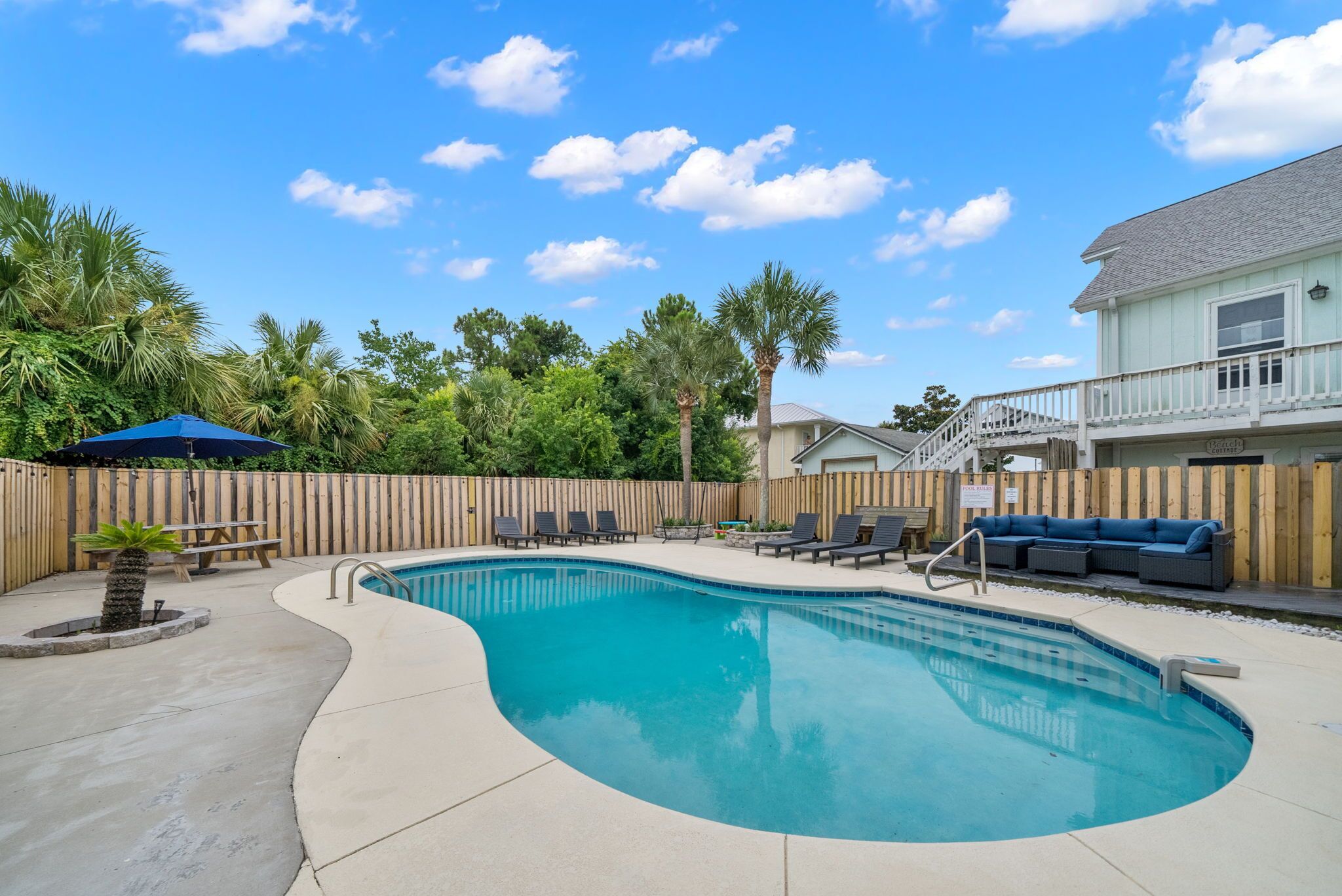 A backyard with a swimming pool, lounge chairs, a wooden fence, and a house with a balcony.