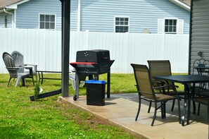 Un patio con una parrilla, sillas y una mesa.