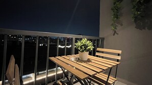 A balcony with a wooden table and chairs, a potted plant, and a view of the city at night. - M&C Departamento República 815 (Santiago)
