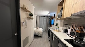 A compact hotel room with a kitchenette, a bed with a rolled towel, a phone, and a TV on the wall. - M&C Departamento República 815 (Santiago)