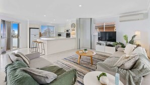 A modern living room with a sofa, coffee table, and a view of the kitchen. - Sunrise on the Bay | Ocean Views & Beach (Malua Bay)