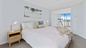 A bedroom with a bed, nightstands, a ceiling fan, a painting, and a balcony view. - Sunrise on the Bay | Ocean Views & Beach (Malua Bay)