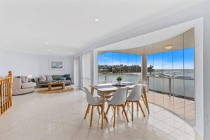 A spacious living area with a balcony, a dining table, and a sofa. - Sunrise on the Bay | Ocean Views & Beach (Malua Bay)