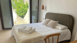 A neatly made bed with white linens and folded towels, a wooden chair, and a view of greenery through a large window. - HOTEL SES TERRISSES (Palafrugell)