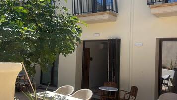 Un patio con mesas al aire libre, una planta grande en maceta y un edificio con balcones.