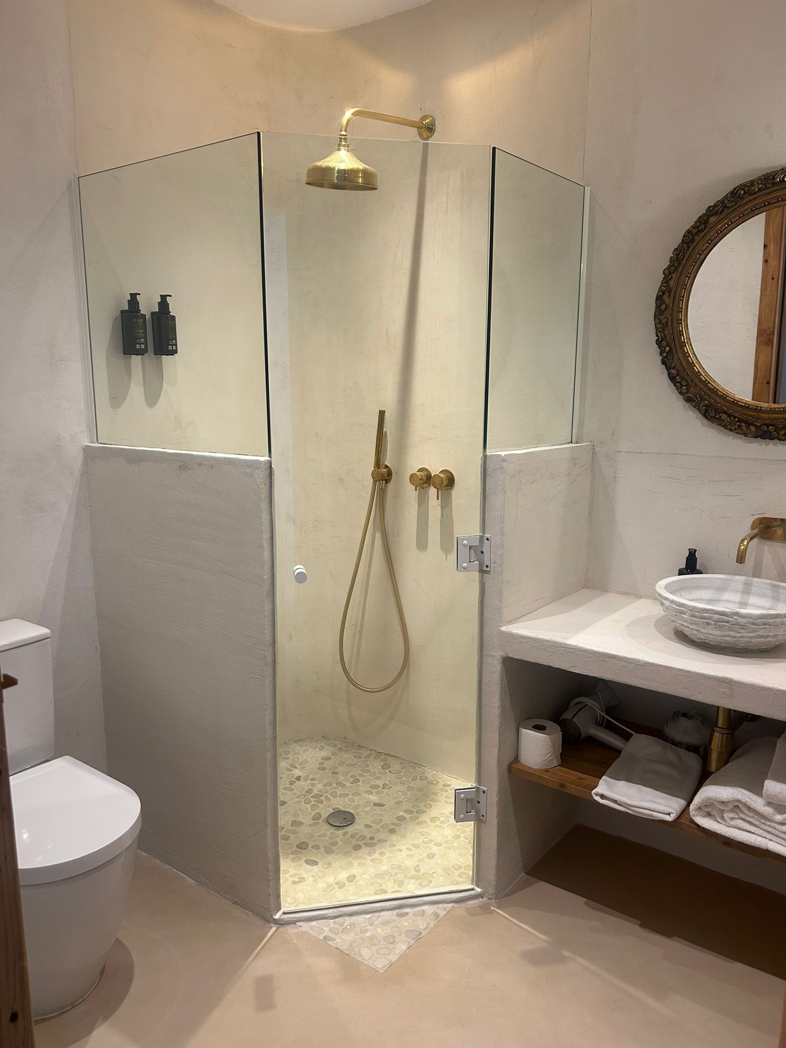 Un baño moderno con ducha de vidrio, un lavamanos blanco con cuenco y un espejo con marco ornamentado.