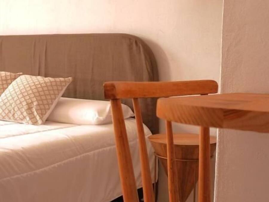 A bedroom with a bed, a wooden chair, and a hanging light fixture.
