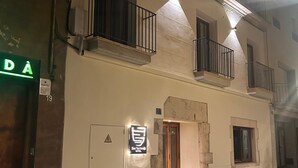 A building with a sign indicating it is a hotel, featuring a balcony with a railing, a door with a window, and a small plant outside. - HOTEL SES TERRISSES (Palafrugell)