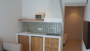 A compact living space with a kitchenette, a sofa, a wooden table, and a TV mounted on the wall. - HOTEL SES TERRISSES (Palafrugell)