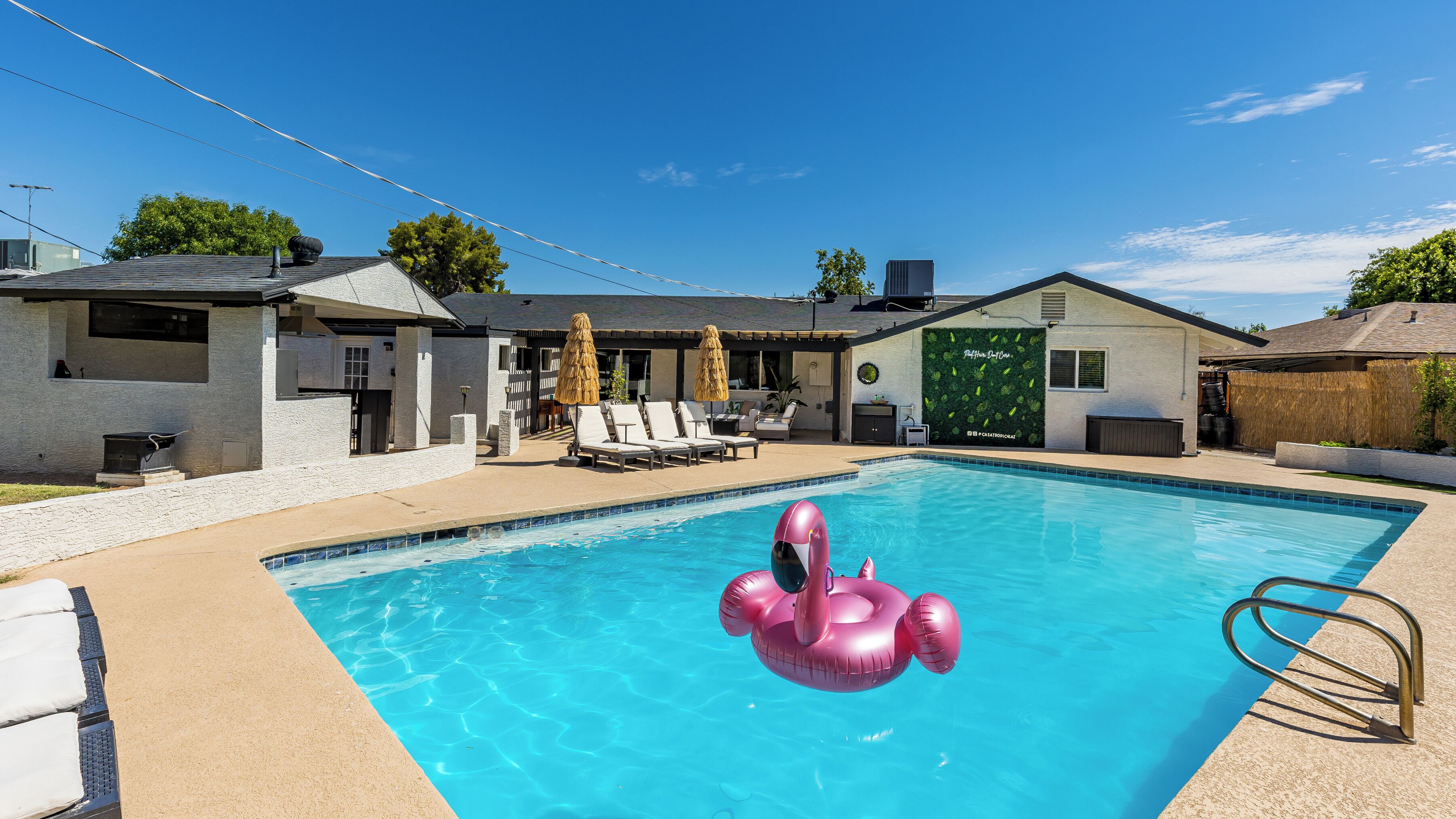 Una piscina con un flotador en forma de flamenco rosa, sillas de descanso y un área de patio techada.