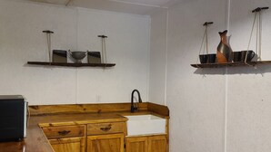A compact kitchen with wooden cabinets, a white sink, and two wall-mounted shelves with decorative items.
