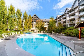 A swimming pool with lounge chairs and a building with balconies in the background. - Ski-In/Ski-Out | On the Mountain! w/ Pool & Hot Tubs (Whistler)