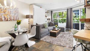 A modern living room with a grey sofa, a coffee table, and a dining area with a glass table and chairs.