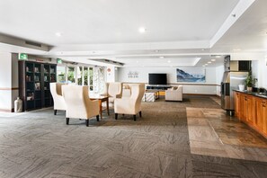A spacious lobby with a high ceiling, a seating area with chairs, a television, a kitchen area with a refrigerator, and a bookshelf. - Ski-In/Ski-Out | On the Mountain! w/ Pool & Hot Tubs (Whistler)