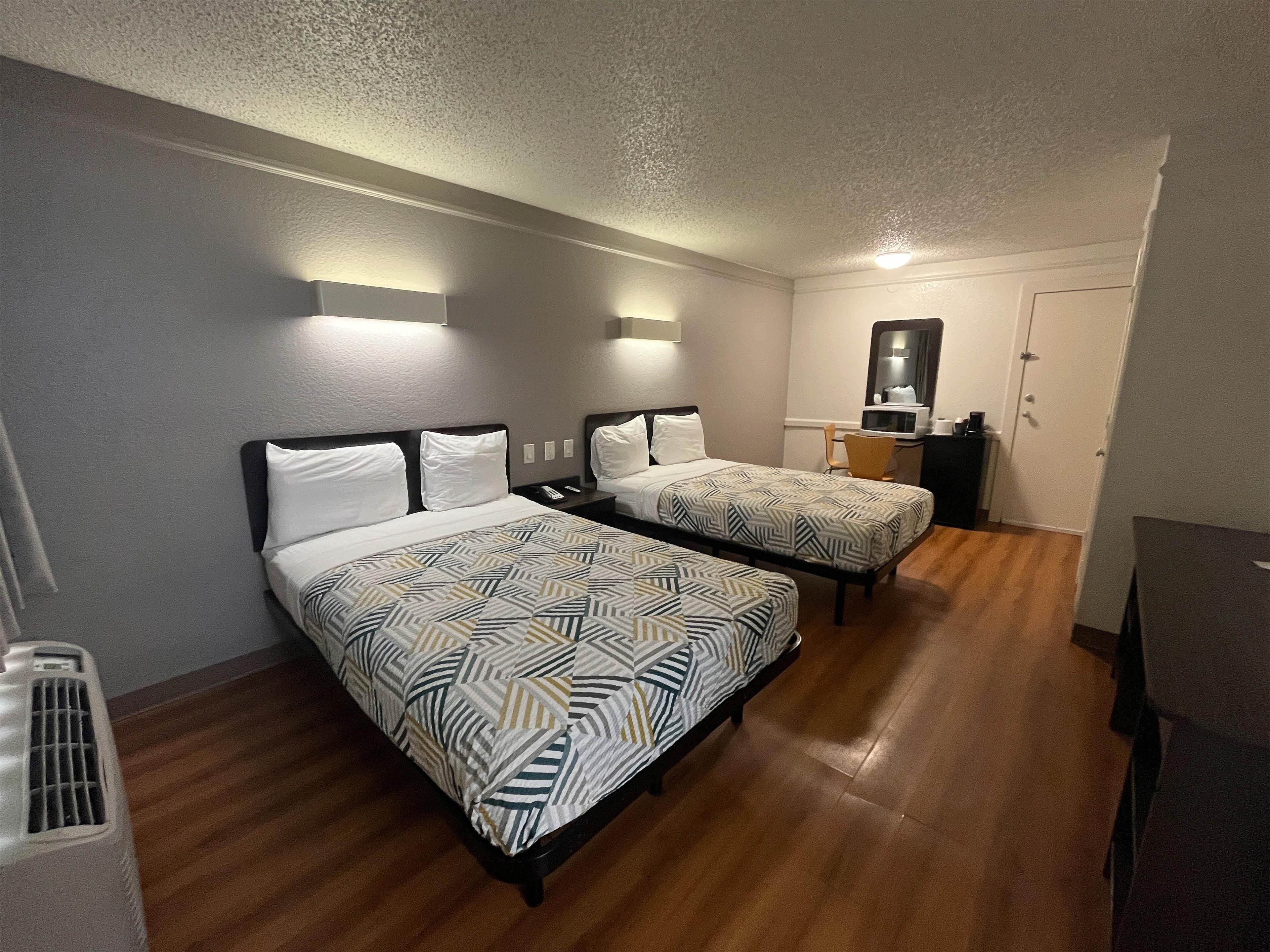 A hotel room with two beds, a desk, a chair, a microwave, and a mirror.