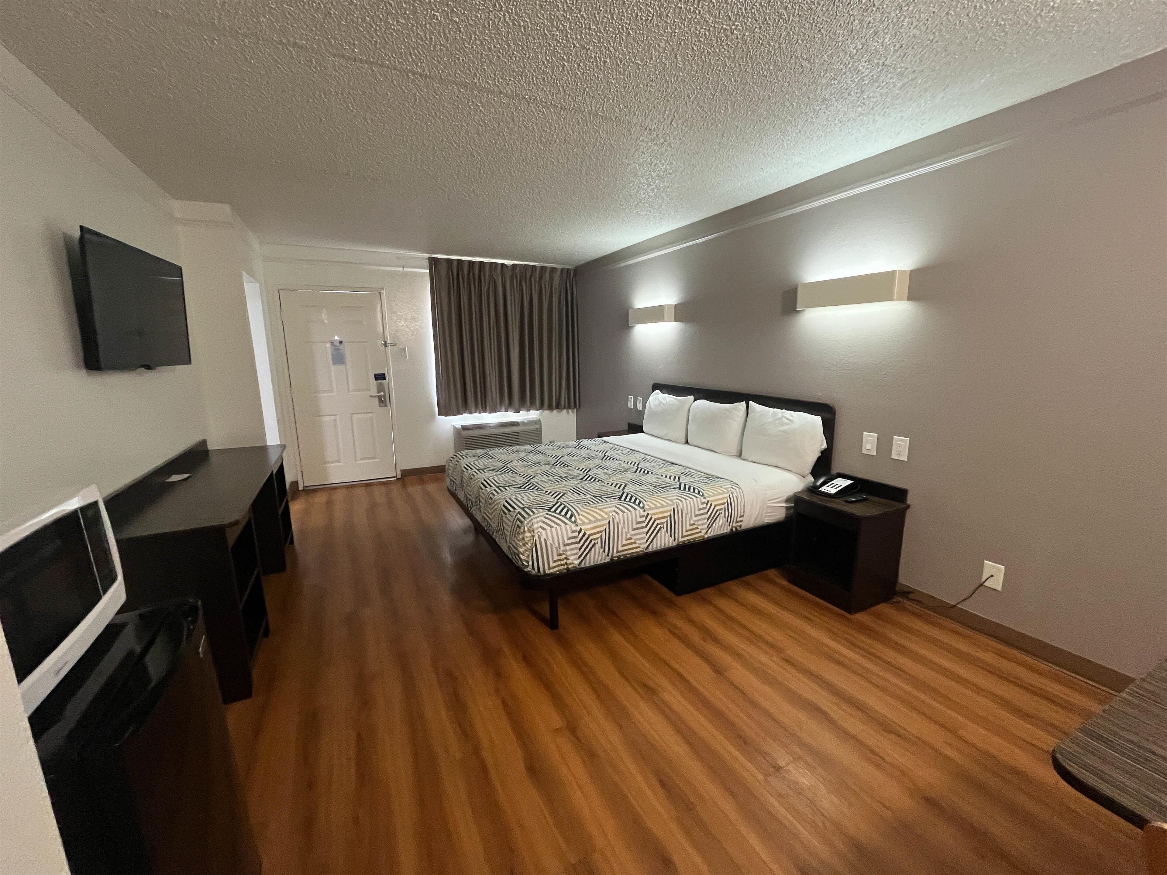 A hotel room with a bed, bedside table, TV, and a desk.