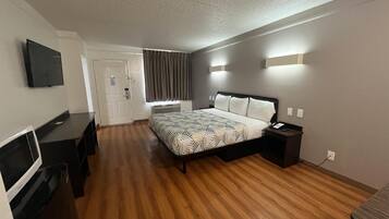 A hotel room with a bed, bedside table, TV, and a desk.