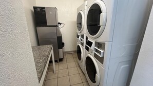 A laundry room with stacked front-loading washers and dryers, a countertop, and a wall-mounted heater. - Studio 6 Suites Euless, Tx – Dfw West (Euless)