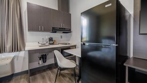 Une cuisine compacte équipée d’un réfrigérateur intégré, d’une machine à café et d’une chaise blanche.