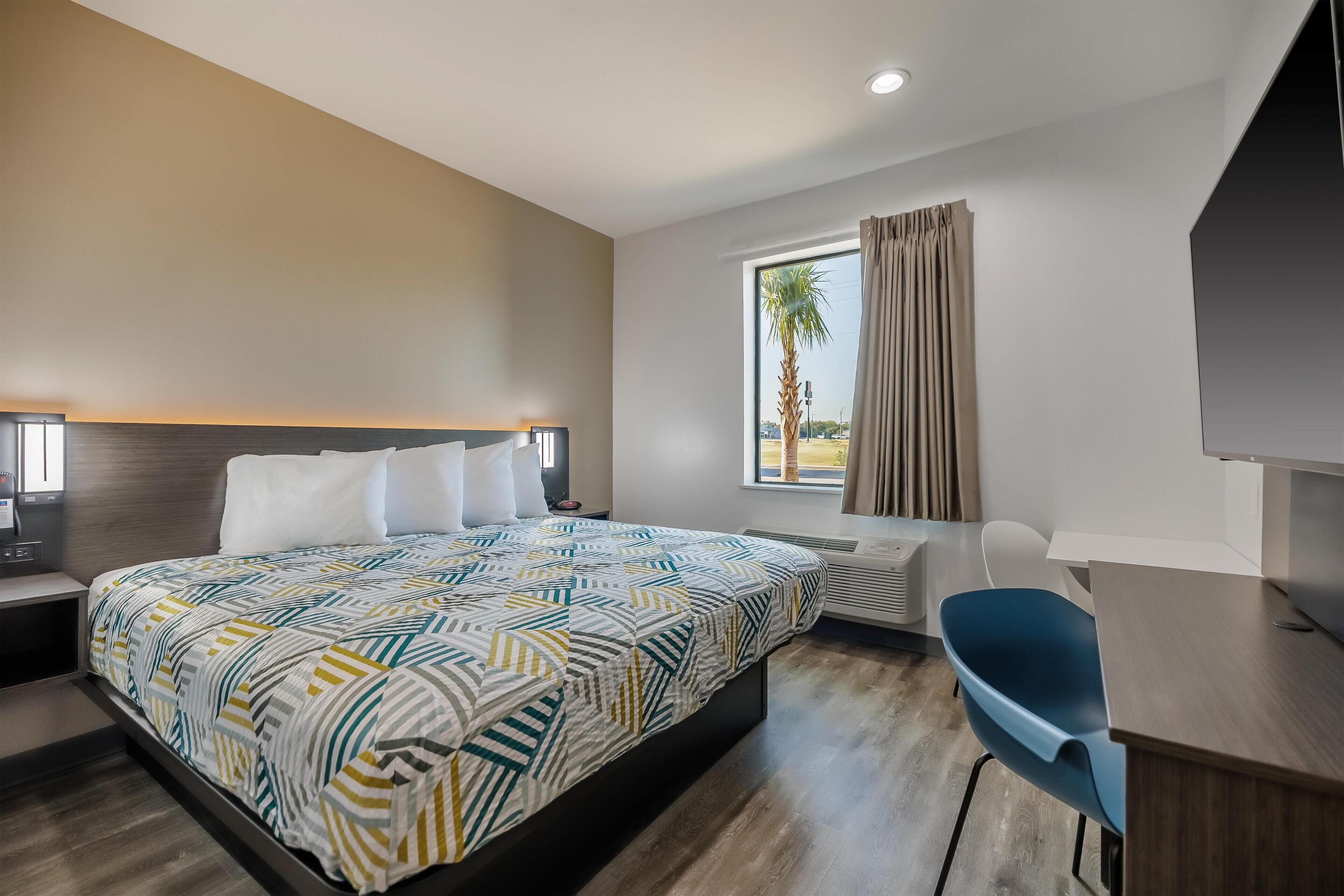 Ein modernes Hotelzimmer mit einem großen Bett, einem Schreibtisch, einem Sessel und einem Fernseher.